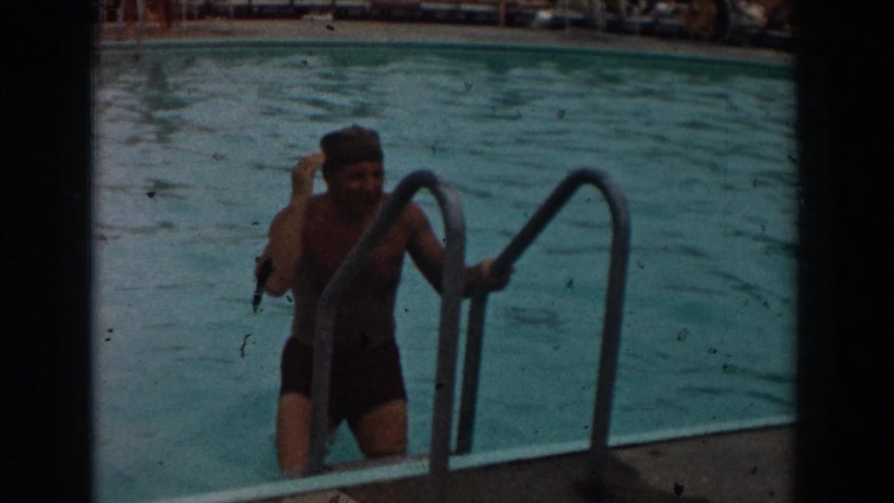 Man wearing a swim cap steps down the pool ladder into the water.