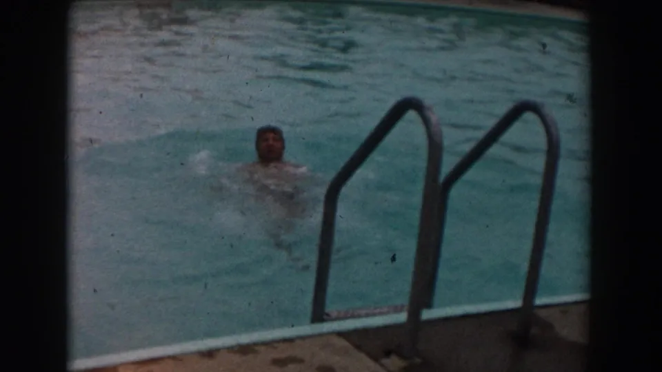 The swimmer moves away from the ladder across the outdoor pool, partly submerged in softly faded 8mm color.