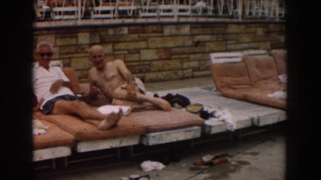 Two older men reclining on poolside lounge chairs near a stone wall.