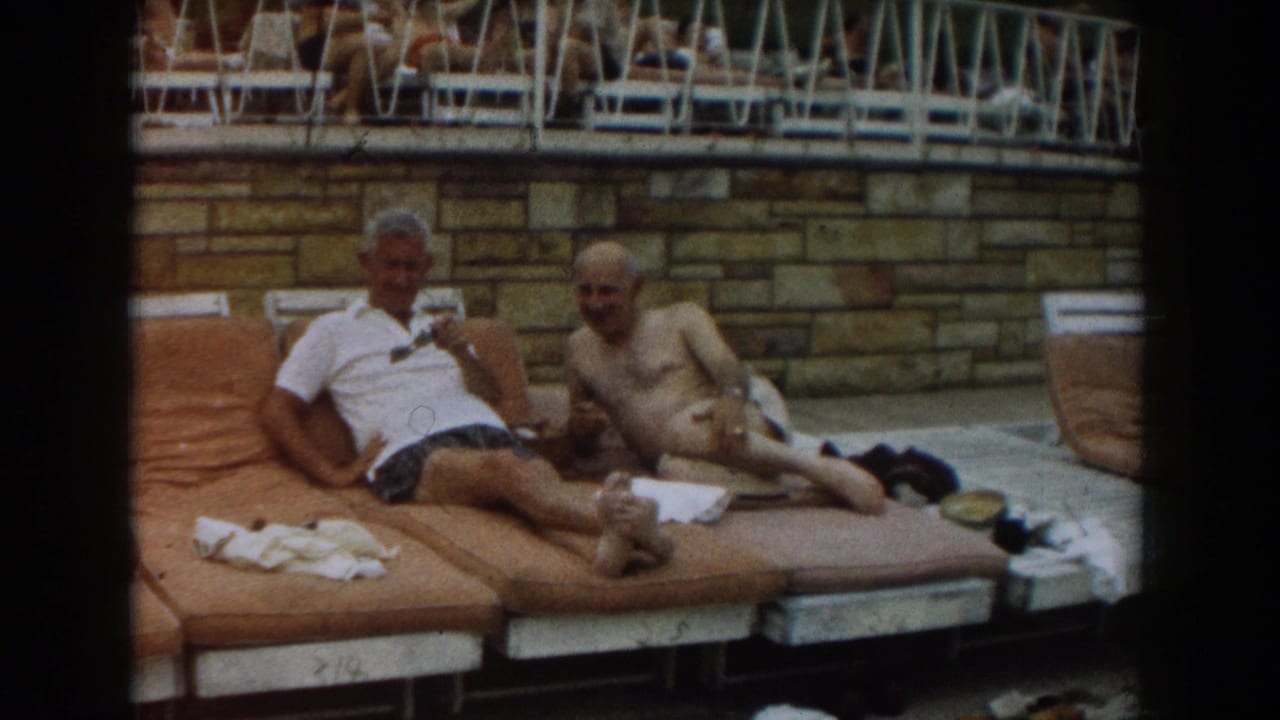 Two men reclining on tan lounge chairs beside a swimming pool.