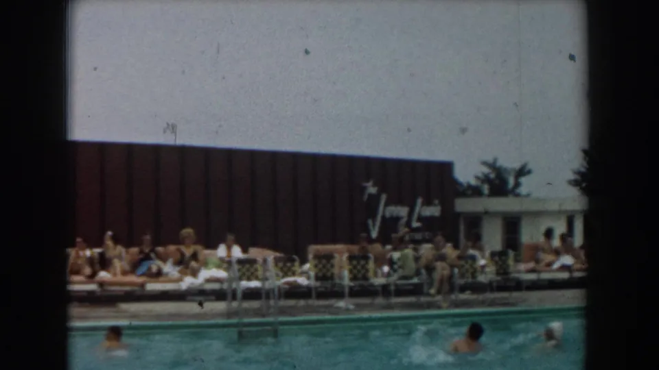 1961 Los Angeles pool scene with adults on lounge chairs, swimmers in the water, a pool ladder, and the Jerry Lewis sign visible behind them.