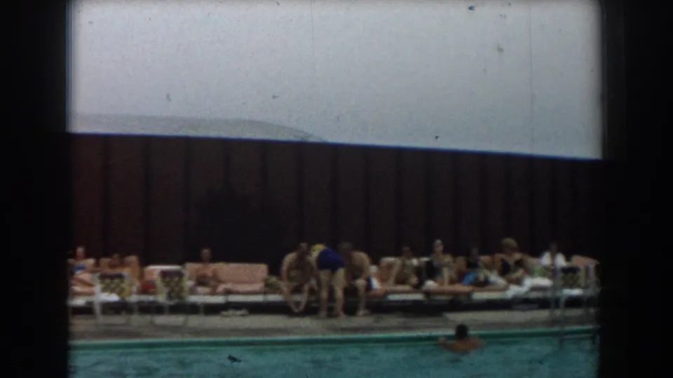 1961 Los Angeles poolside frame showing adults reclining on lounge chairs, one person bending near the deck, and a swimmer in the foreground.