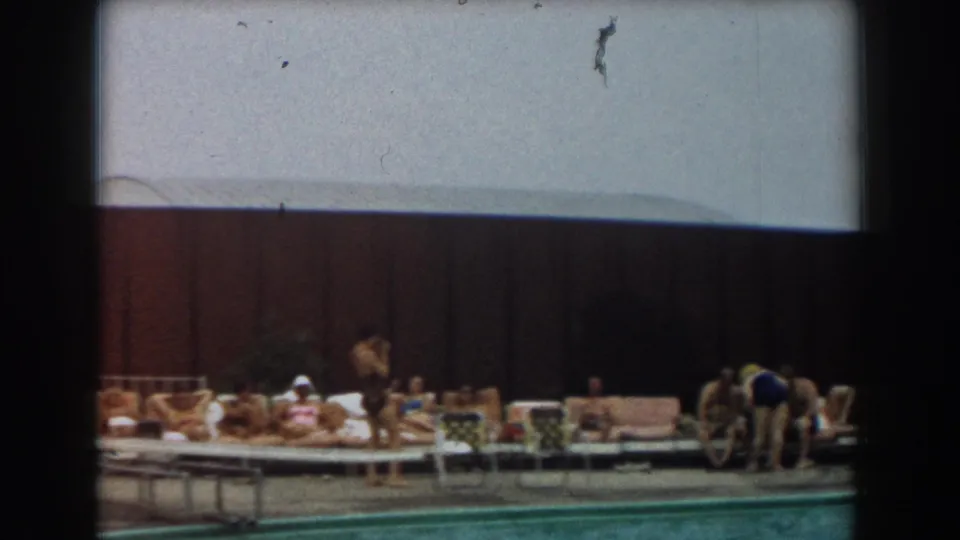 1961 Los Angeles 8mm poolside view with adults on lounge chairs, a person bending near the deck, and a swimmer at the lower edge.