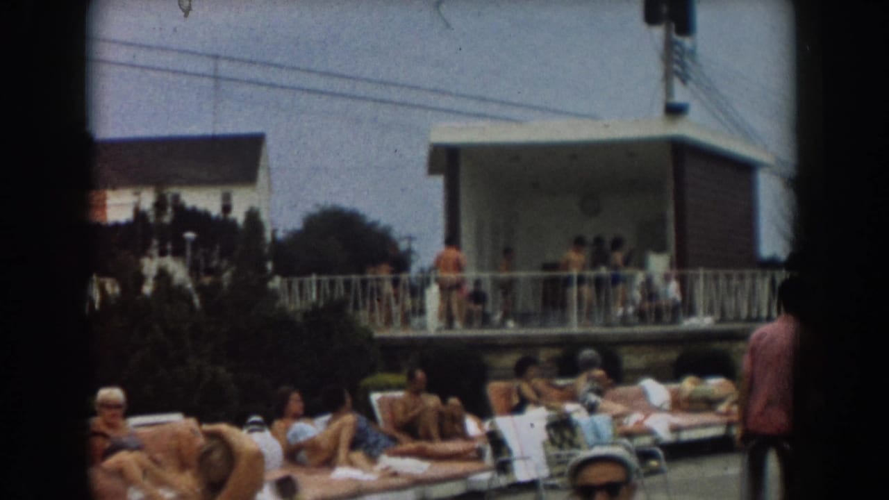 Sunbathers relax on lounge chairs near a pool deck and light-colored building.