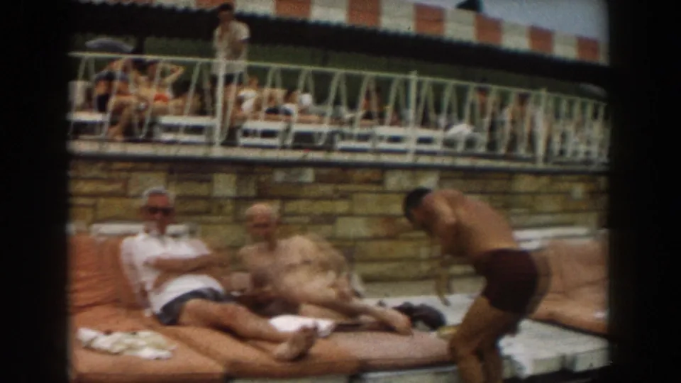 1961 Los Angeles poolside view with reclining adults on lounge cushions and a man in dark swim trunks bending nearby.