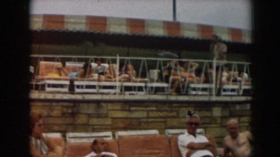 1961 Los Angeles poolside scene with adults reclining below a raised deck lined with lounge chairs and a striped awning.