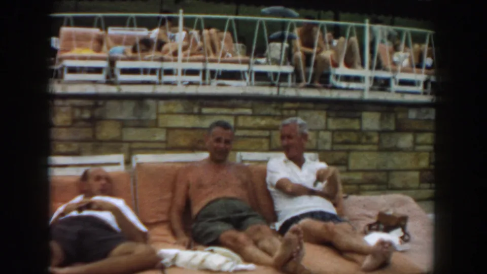 1961 Los Angeles poolside frame showing adults reclining and sitting on orange lounge chairs below a busy raised sun deck.
