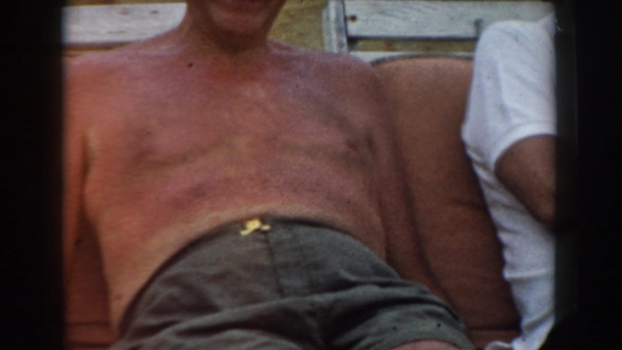 Shirtless older man reclines on outdoor seating beside a partially visible companion.