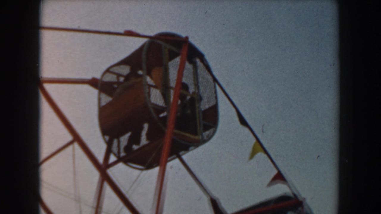 Low-angle view of a red Ferris wheel gondola with seated passengers against the sky.