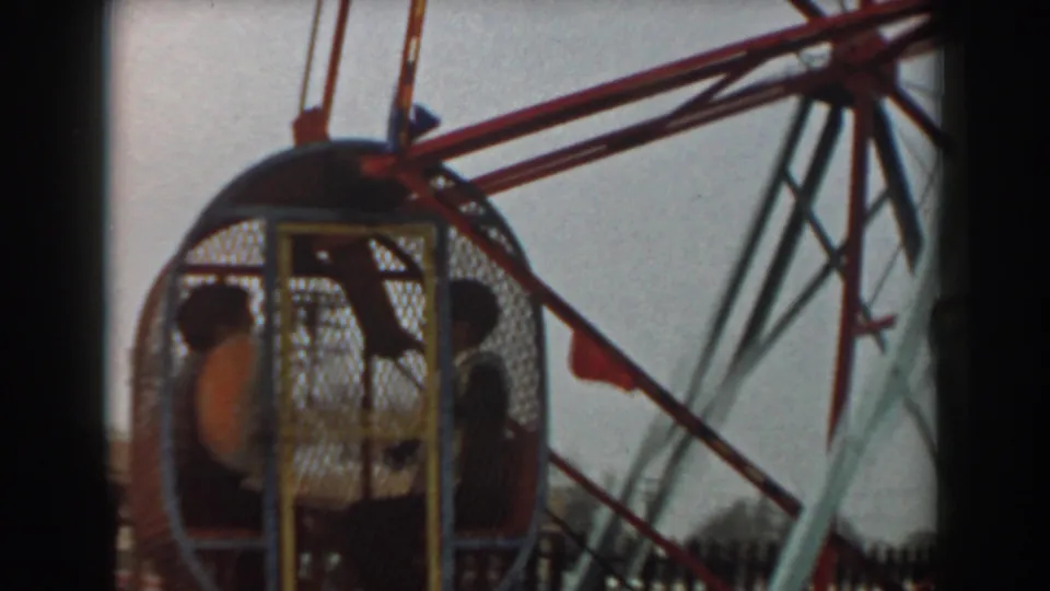 1961 Los Angeles frame showing a red Ferris wheel car with passengers, wheel spokes, and a small flag near the ride structure.