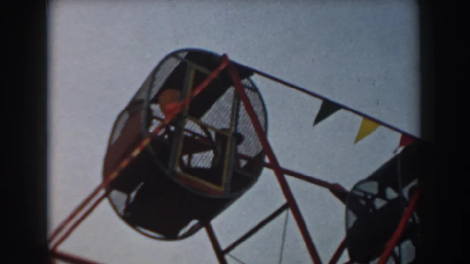 1961 Los Angeles 8mm frame showing children inside a round mesh cage on a small amusement park wheel ride.