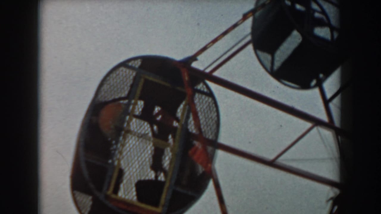 Low-angle 8mm view of children seated inside an enclosed amusement ride cage in Los Angeles, 1961.