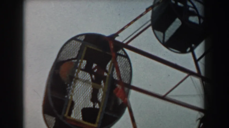 Low-angle 8mm view of children seated inside an enclosed amusement ride cage in Los Angeles, 1961.