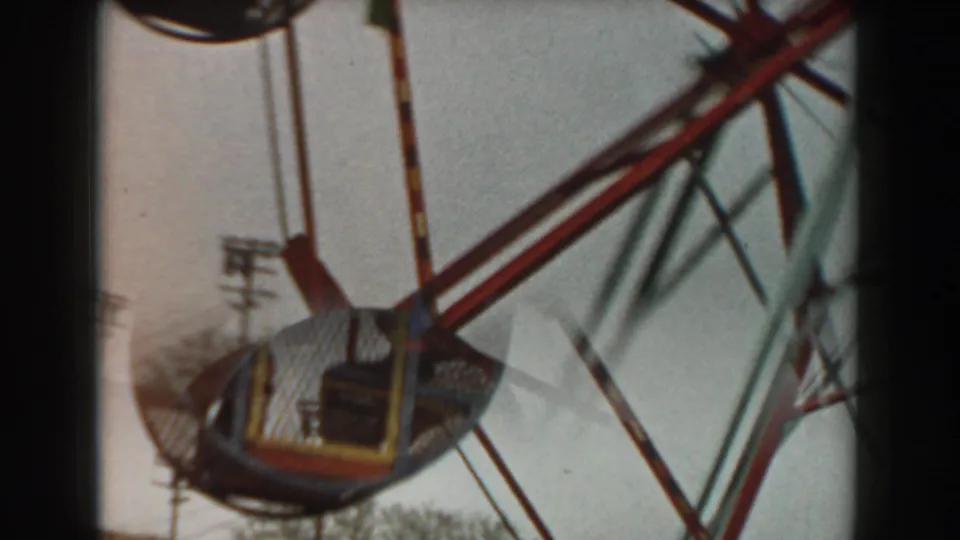 Home-movie frame of the cage wheel ride structure with a lower passenger cage and blurred supports against the sky.
