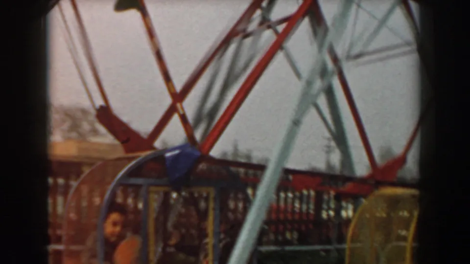 1961 Los Angeles amusement park frame showing the cage wheel supports, mesh fencing, and a child partly visible near the midway.