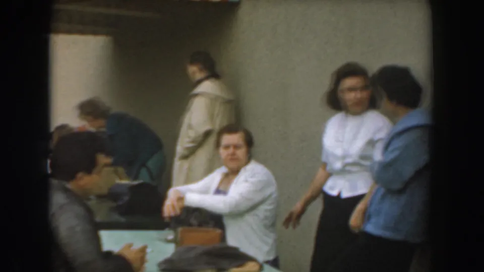 Home-movie frame from a Los Angeles indoor gathering in 1961, with seated adults and a standing woman in a white blouse.