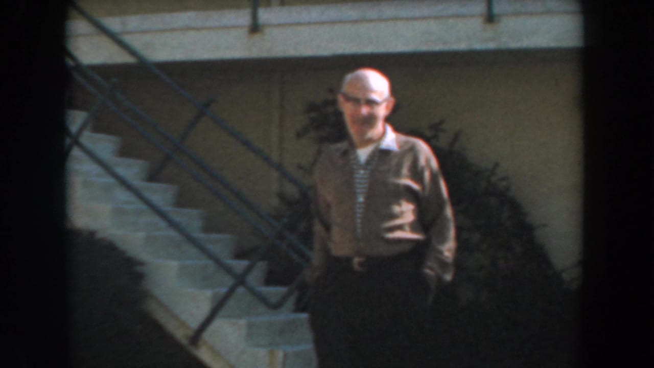Man walks closer with hands in pockets beside exterior stairs and a metal railing.