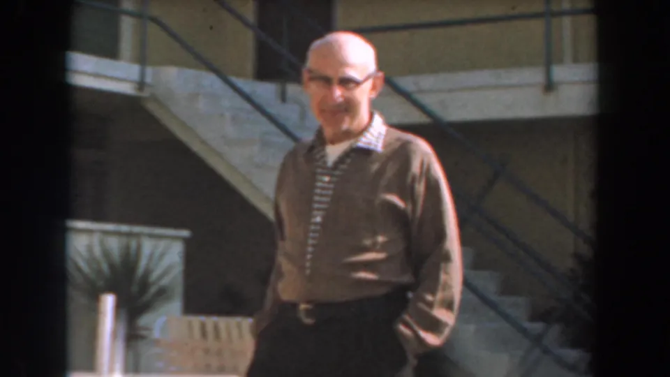 A closer 8mm frame shows the man smiling or laughing toward the camera as he walks outside the building.