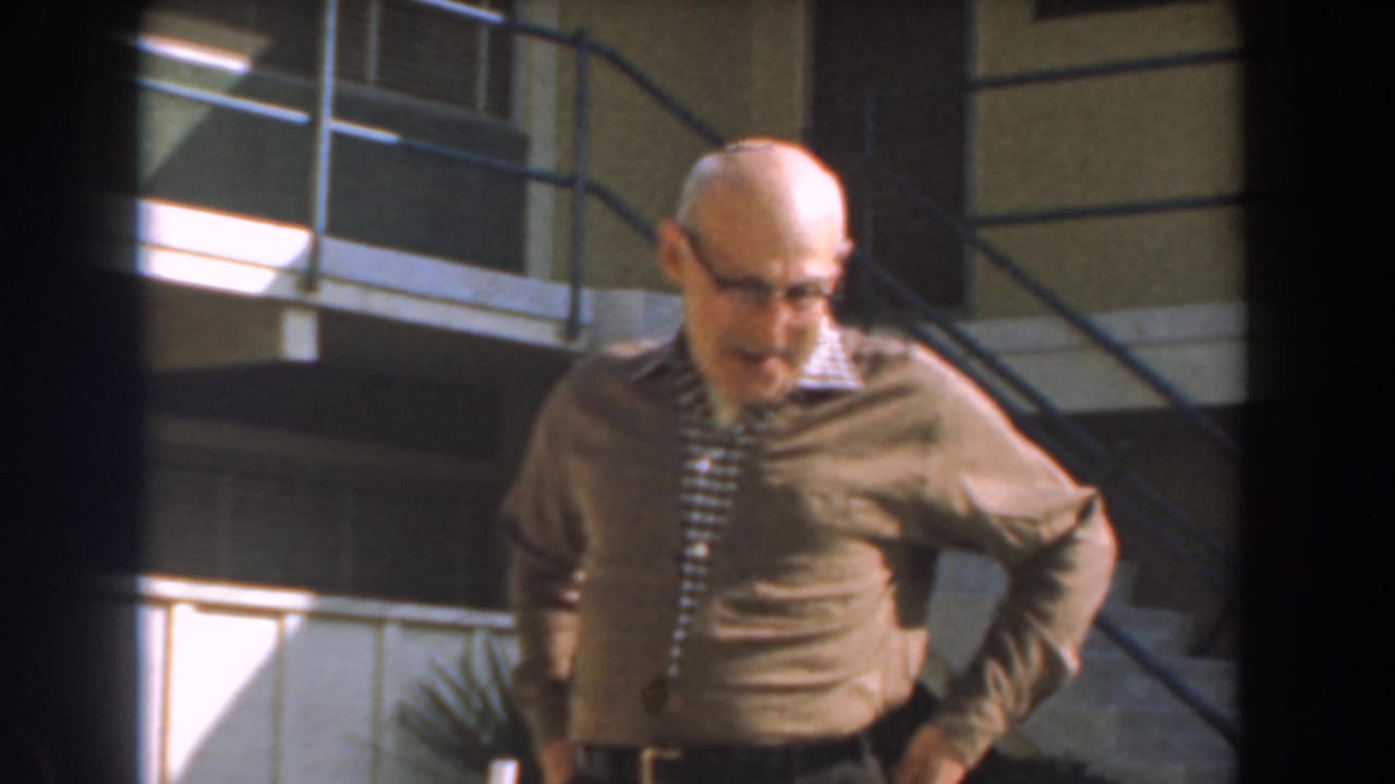 Older man in glasses stands near exterior stairs with hands at his waist.