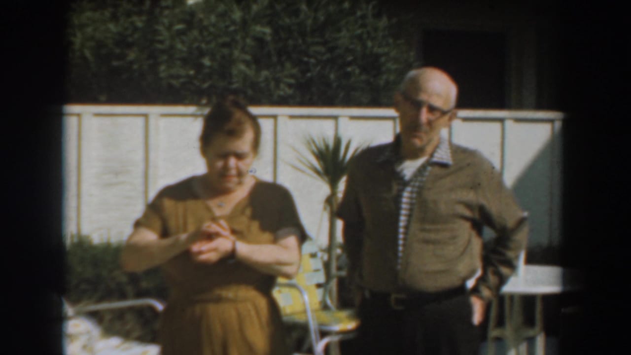 Woman looks down at her hands while a man stands beside her near patio furniture.