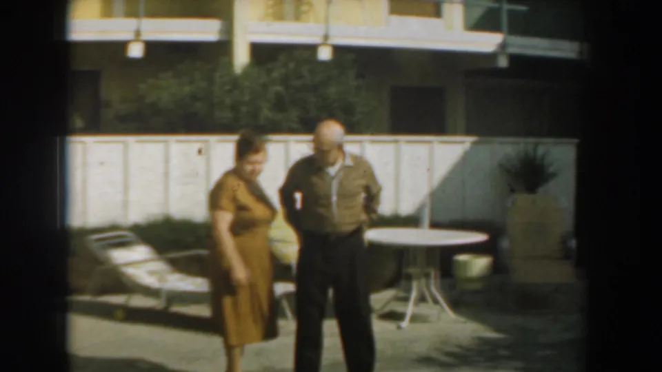 A wider 1961 backyard view shows the couple standing on a patio near lounge seating, a round table, and a white fence.