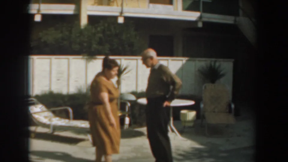 The woman and man face each other in the Los Angeles backyard, framed by patio furniture, a white fence, and garden greenery.