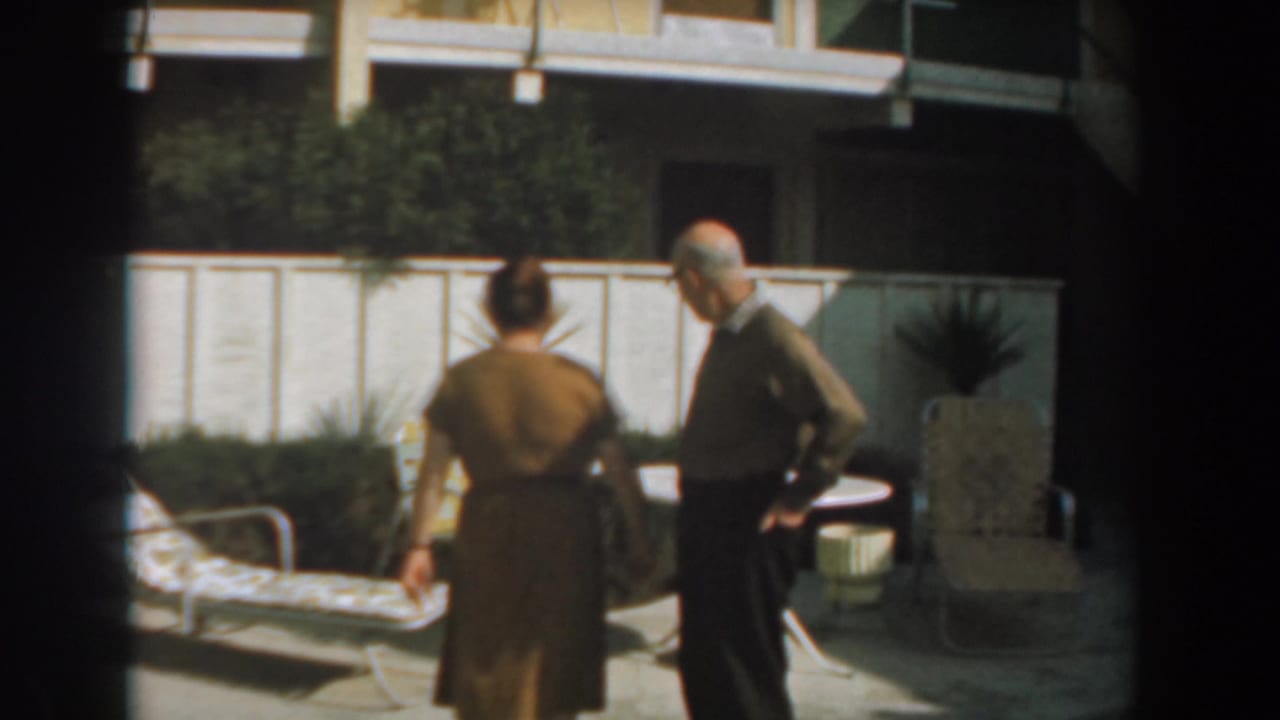 Woman seen from behind while an elderly man stands near a round patio table.
