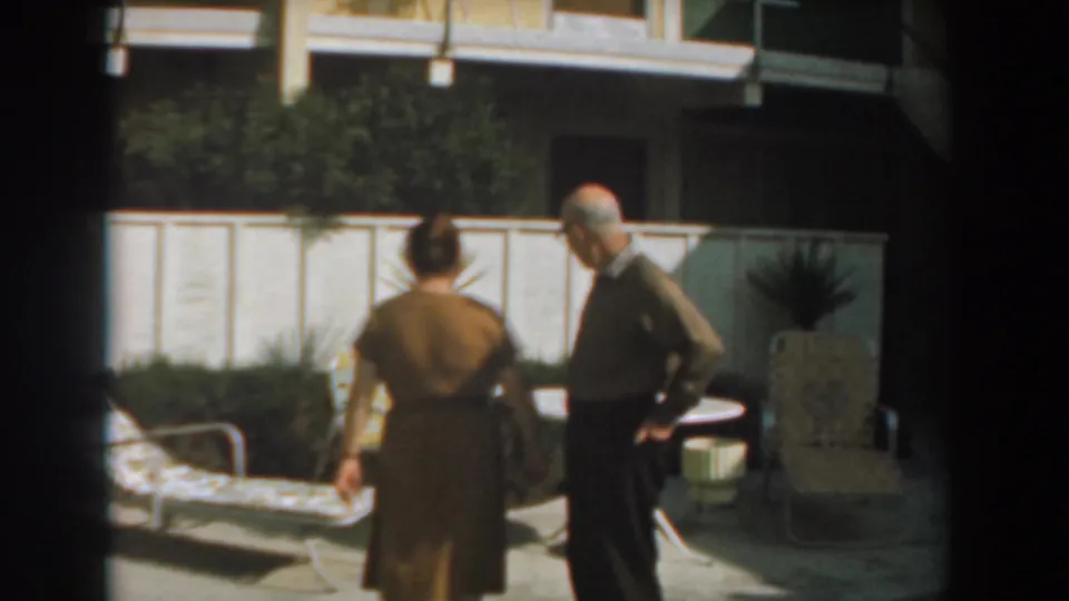 The woman turns away from camera as the elderly man stands by a round patio table in the Los Angeles backyard setting.