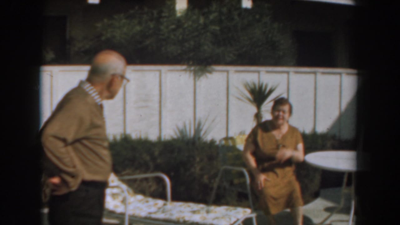 Woman sits near a patio table while an older man faces her in the yard.