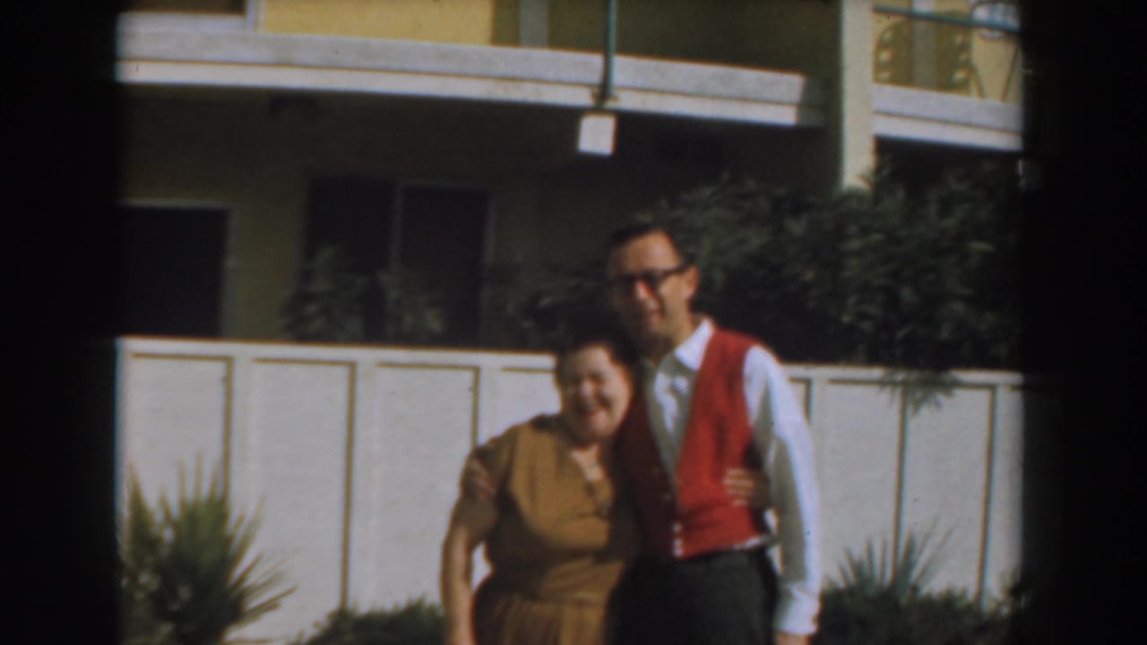 Woman smiling beside a man in a red vest near a white fence.