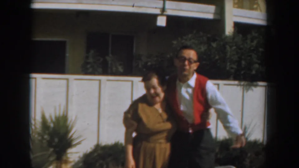The pair remain close together in front of the apartment exterior, framed with soft 8mm color and grain.