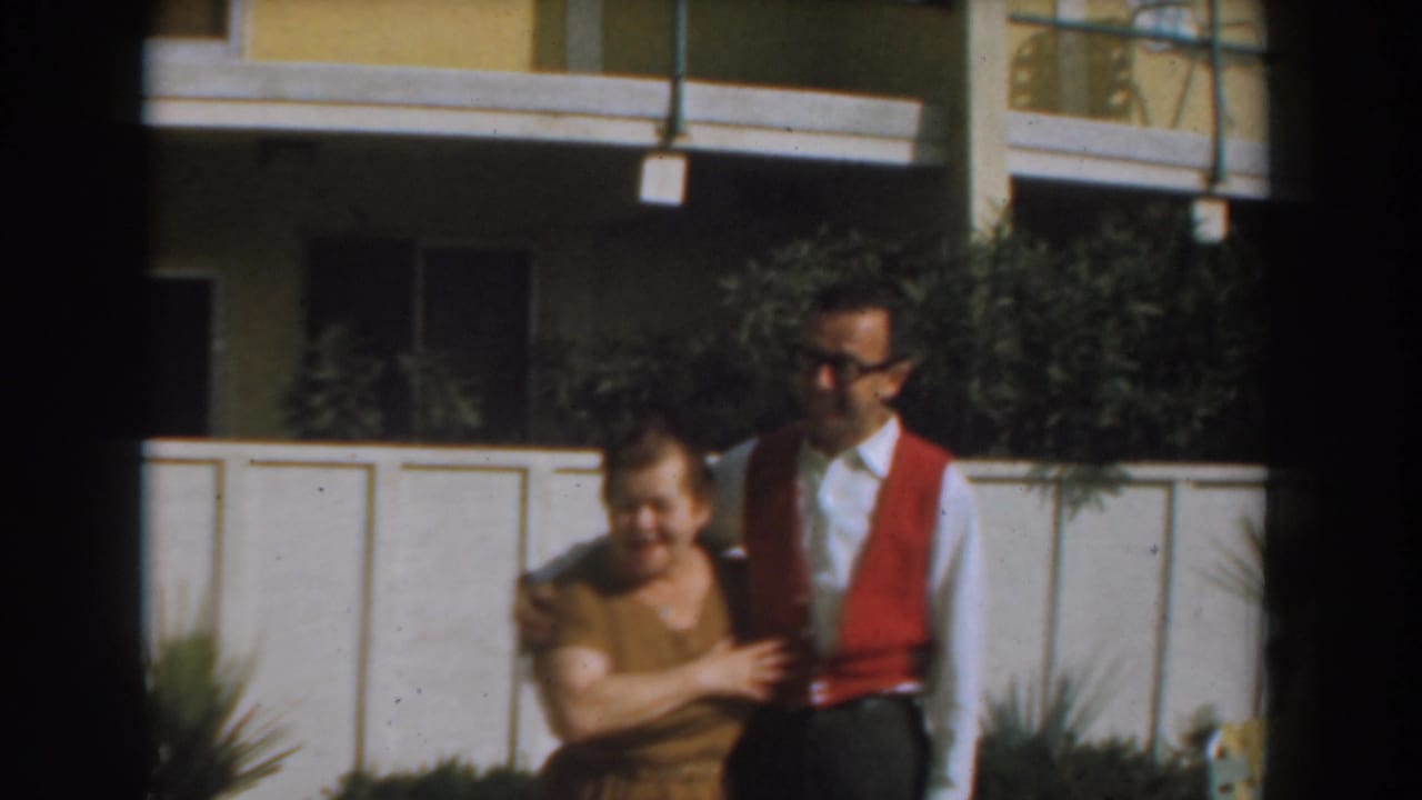 Woman holds the man's arm while they stand near a white fence.