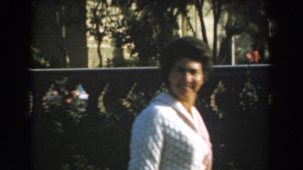 Woman in a white cardigan turns toward the camera in a garden.
