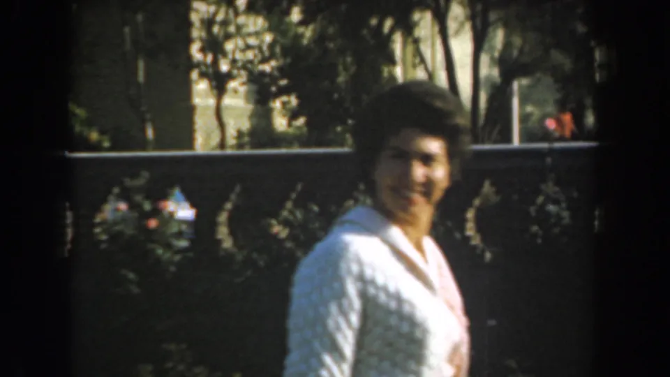 The woman turns toward the camera in a Los Angeles garden, with a dark wall and foliage behind her.