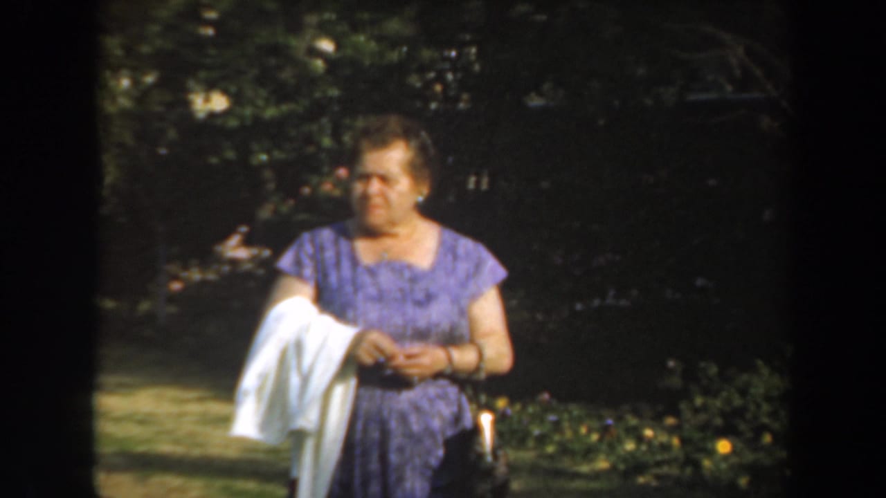 Woman in a purple dress holding a white cloth while standing in a shaded garden.