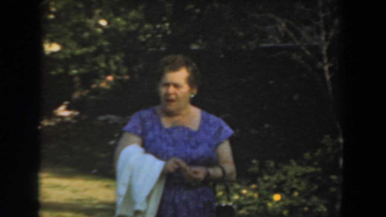 Woman in a purple dress walks through a garden with a white cloth over her arm.