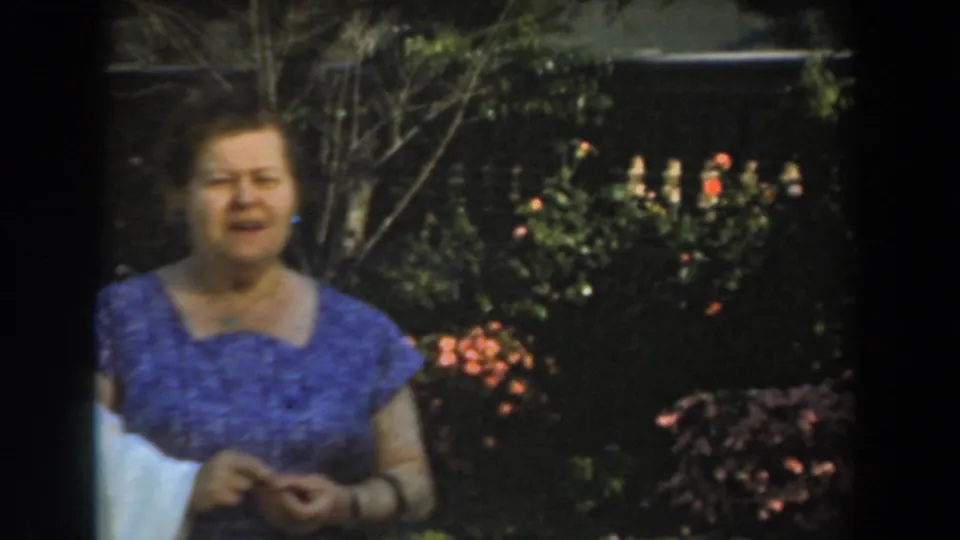 Closer 8mm view of the woman in a purple dress in the Los Angeles garden, framed by shrubs, flowers, and soft sunlight.