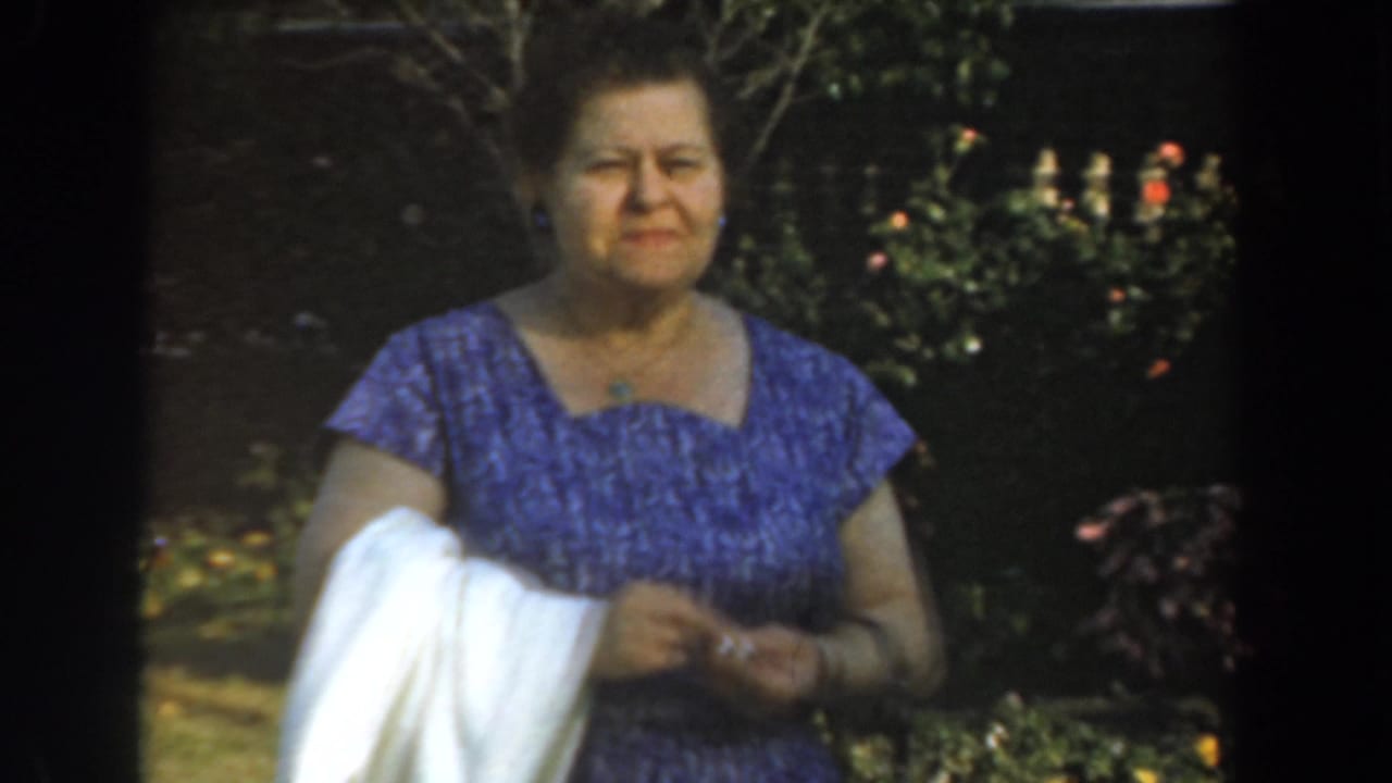 Adult woman in a purple dress holds a white cloth while standing in a sunlit garden.