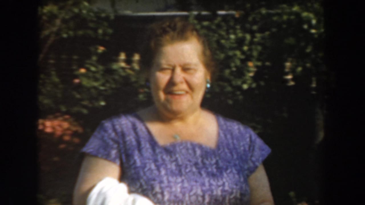 Adult woman smiles toward the camera with garden foliage behind her.