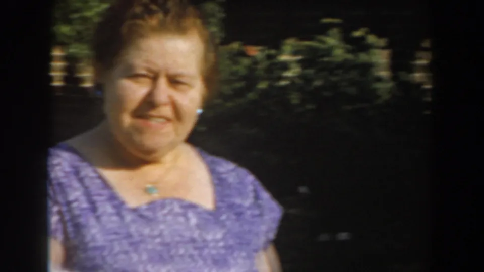 Adult woman in a purple patterned dress looks toward the camera in bright Los Angeles garden light, consistent with 1961 home-movie footage.