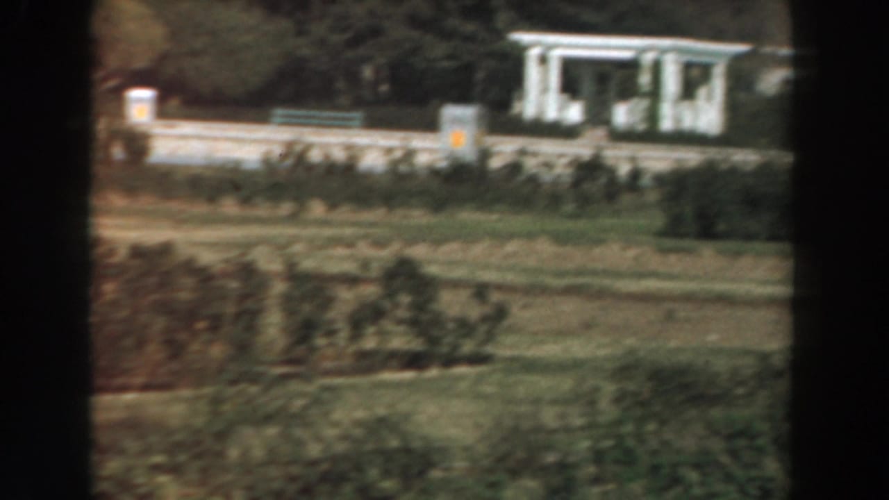 1961 Los Angeles campus-like grounds with a white columned building, clipped hedges, lawn, and a dark film-frame divider.