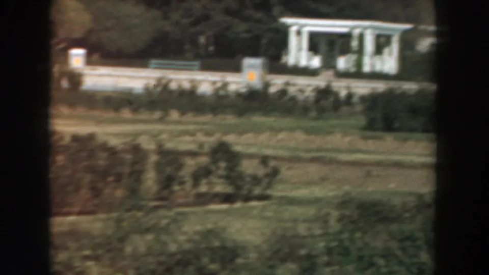 1961 Los Angeles campus-like grounds with a white columned building, clipped hedges, lawn, and a dark film-frame divider.