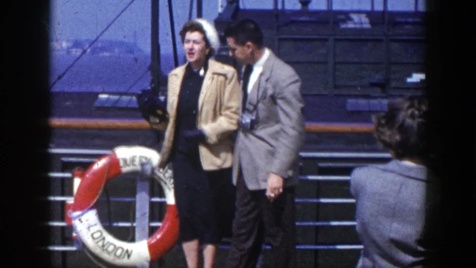 Passengers on a ship deck pass a red-and-white life ring marked Queen of London in 1948 archival home-movie footage.