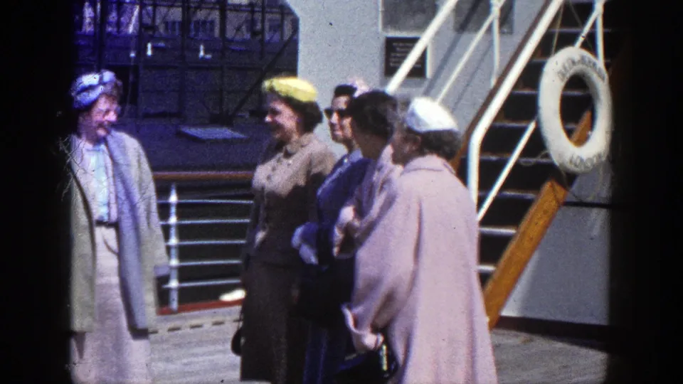 A small group of adults socialize on a ship deck near stairs and a mounted life ring in 1948 New York-linked footage.