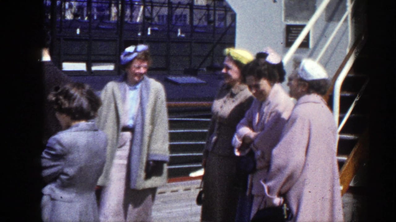 Adults in coats and hats stand on a boat deck near stairs and railings.