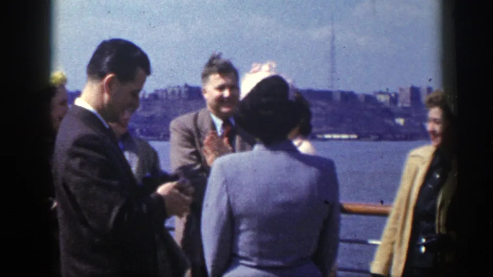A man in a dark suit appears to handle a small item while other adults stand nearby at the New York waterfront in 1948 footage.