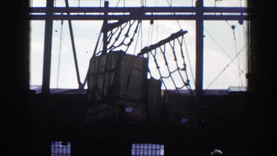 1948 New York 8mm still with netted cargo boxes, crane cables, structural framing, and bright warehouse windows.