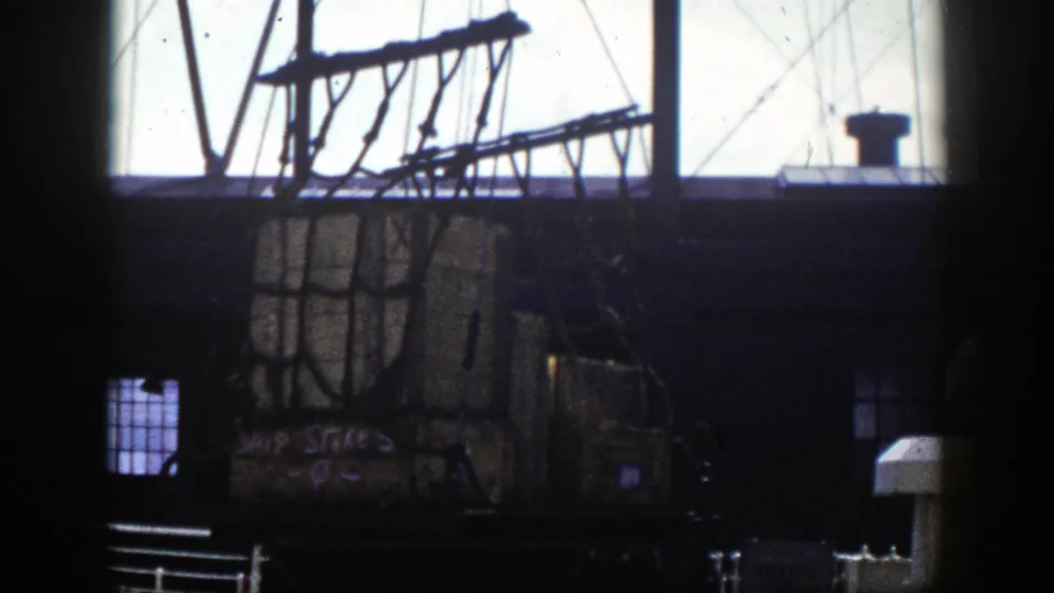 Wooden crates in a cargo net sit near a dock platform, framed by dark interior posts and bright waterfront windows in 1948 New York footage.