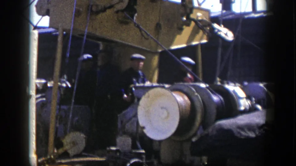 1948 New York factory frame showing workers beside heavy machinery, a round drum, cables, and industrial fixtures.