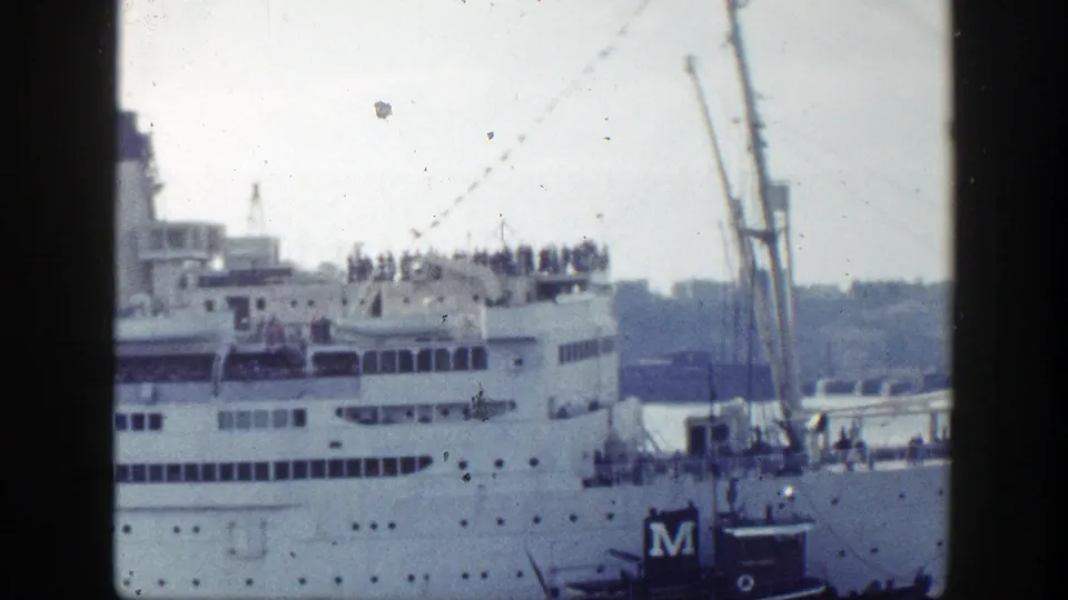 The Atlantic passes through the frame with upper-deck figures, a tugboat marked M, and a muted New York shoreline behind.